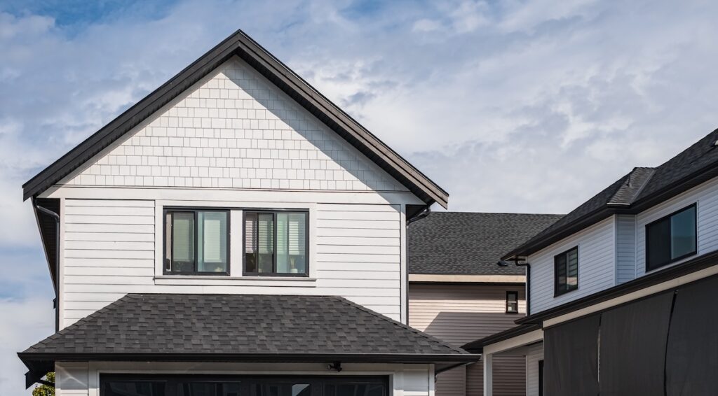 Houses with shingle roof against blue sky. Edge of roof shingles on top of the houses dark asphalt tiles on the roof. 