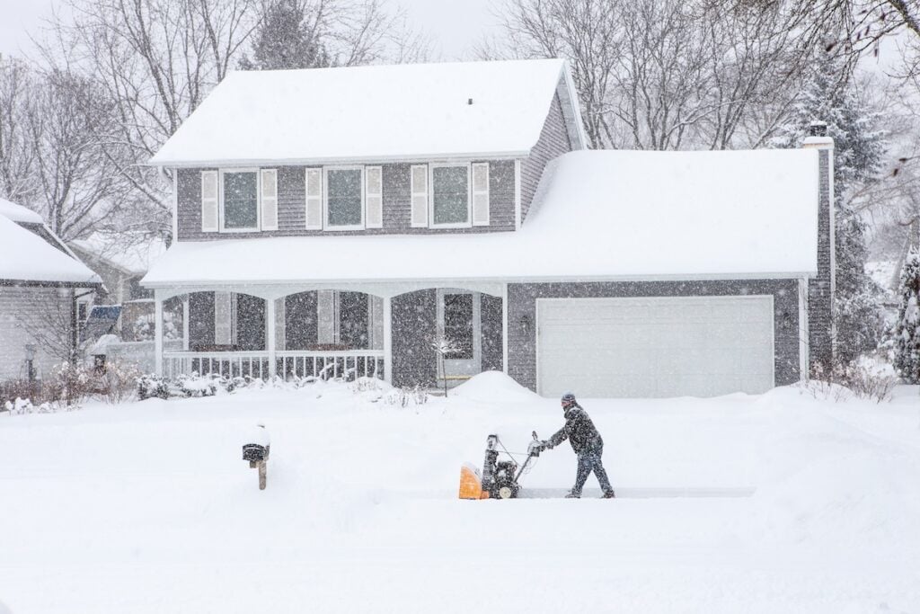 Man using a snowblower to clear his sidewalk and driveway