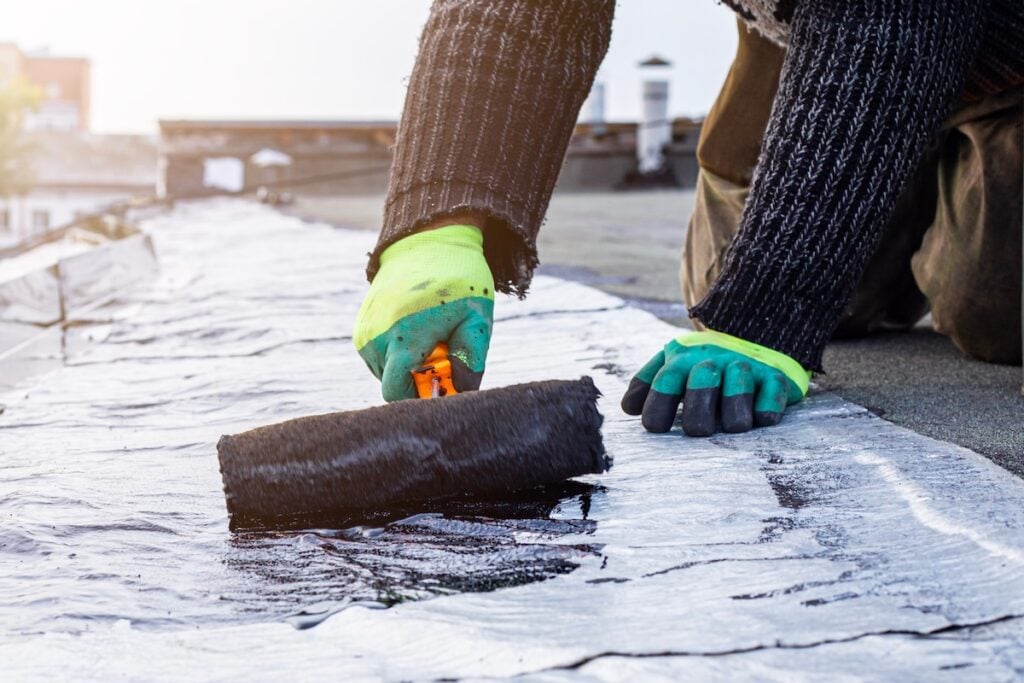 a young worker treats a roof with bitumen primer before applying rolled asphalt roofing using a torch