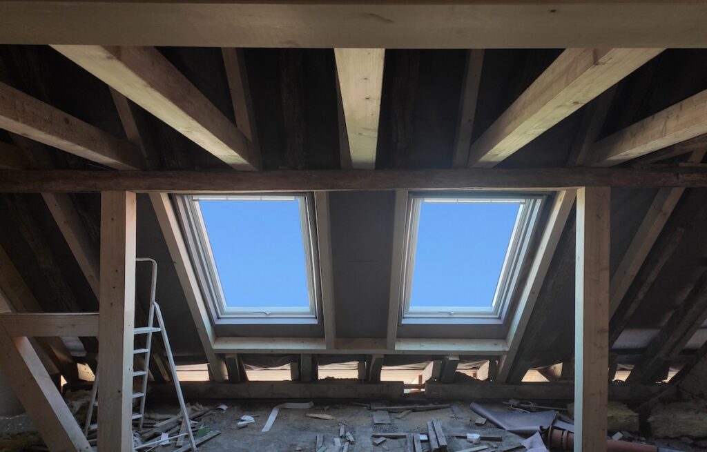 Replacing two outdated windows with new ones in the mansard garret or attic of old house,or private residential building.View from inside.Real construction object..Wooden load-bearing roof beams.Selective focus.Back lighting.
