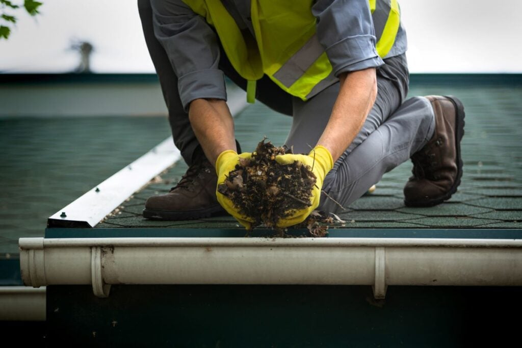 person cleaning debris from half round gutters