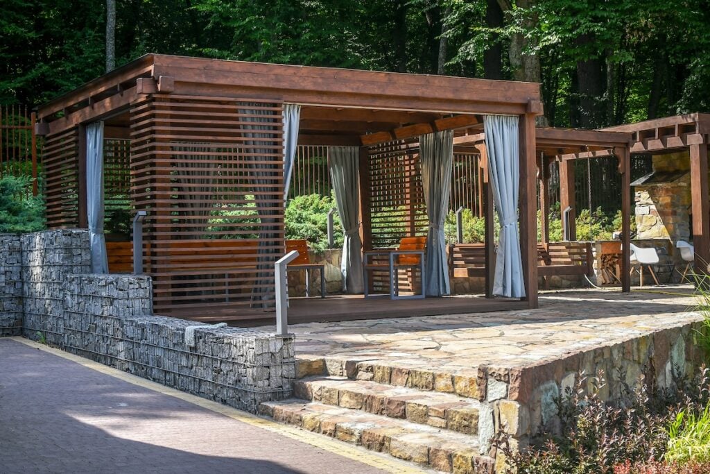 Close up wooden gazebo decorated with gabion elements and natural stone pavement.