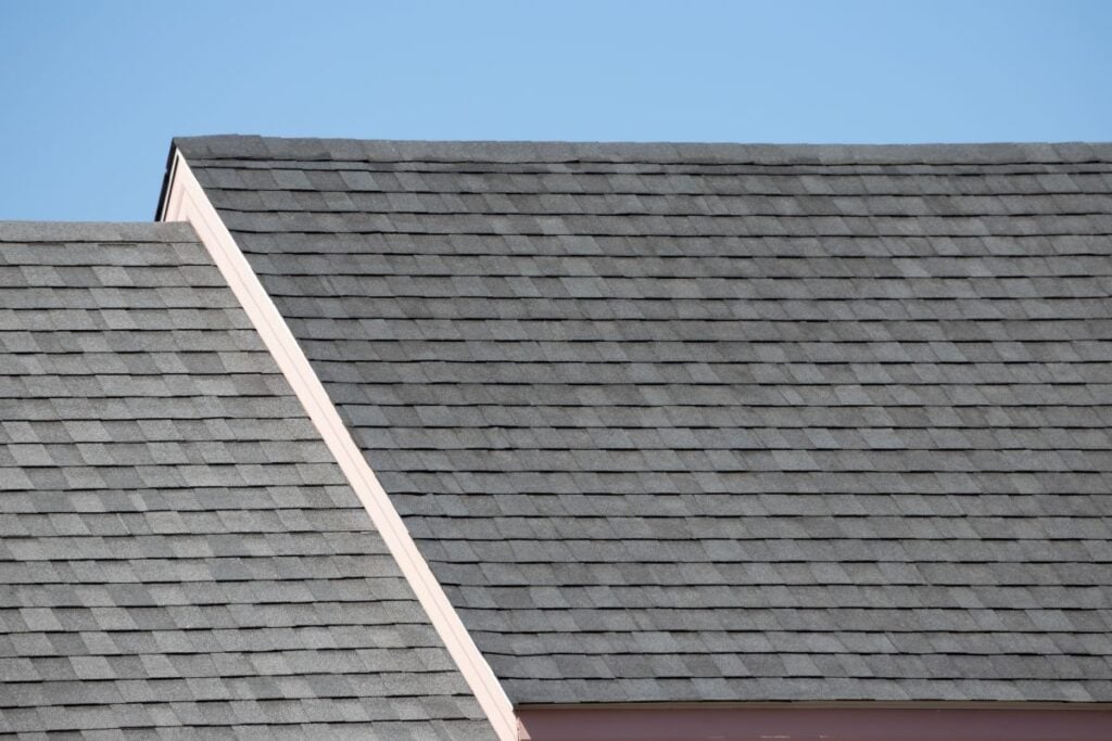 Roof shingles on top of the house against blue sky with cloud, dark asphalt tiles on the roof background.
