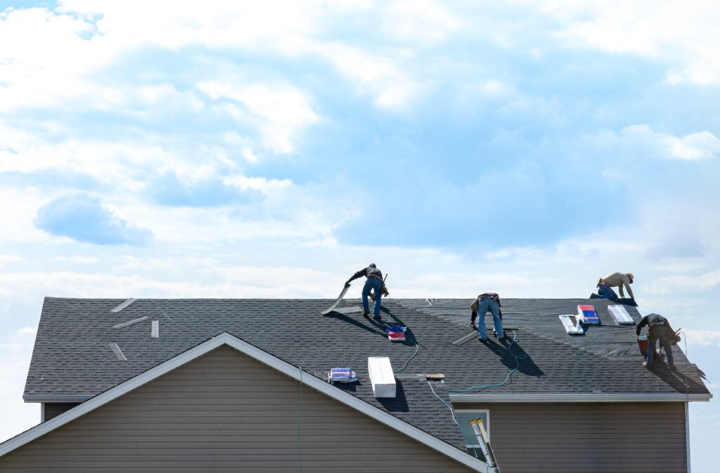 4 construction workers fixing roof against clouds blue sky, install shingles at the top of the house. 