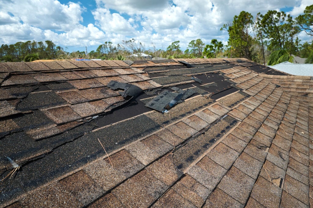 Damaged house roof with missing shingles after hurricane Ian in Florida. 